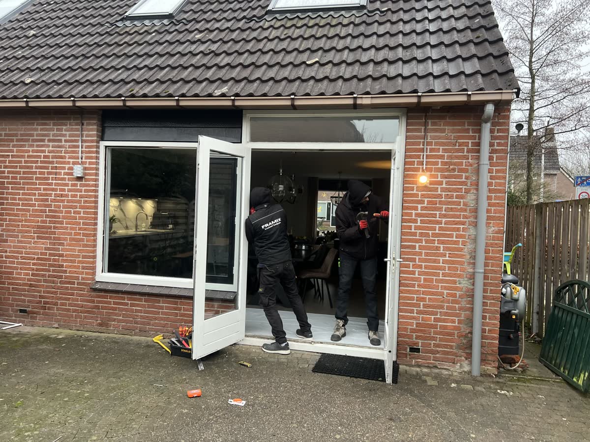 Twee monteurs plaatsen witte openslaande deuren in een bakstenen aanbouw