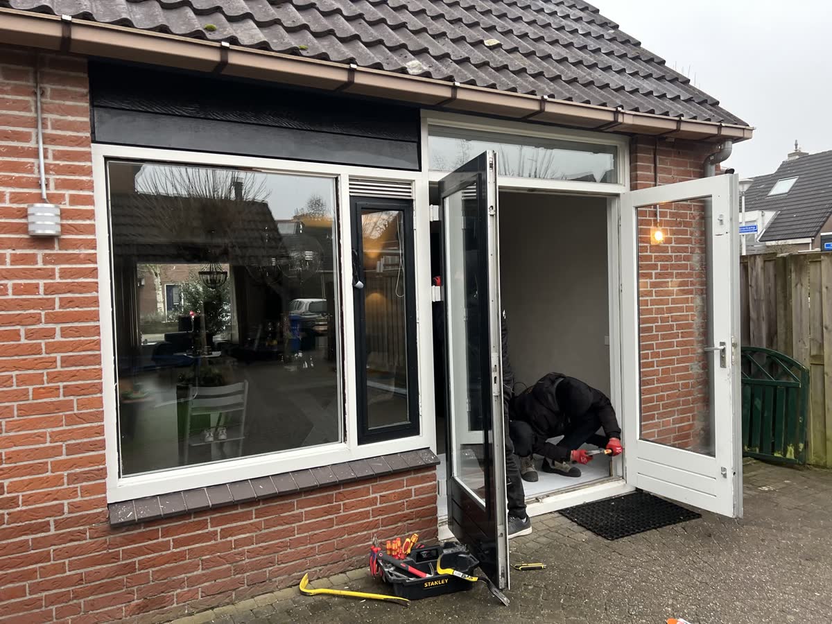 Monteur plaatst een nieuw kozijn in de achtergevel van een bakstenen woning