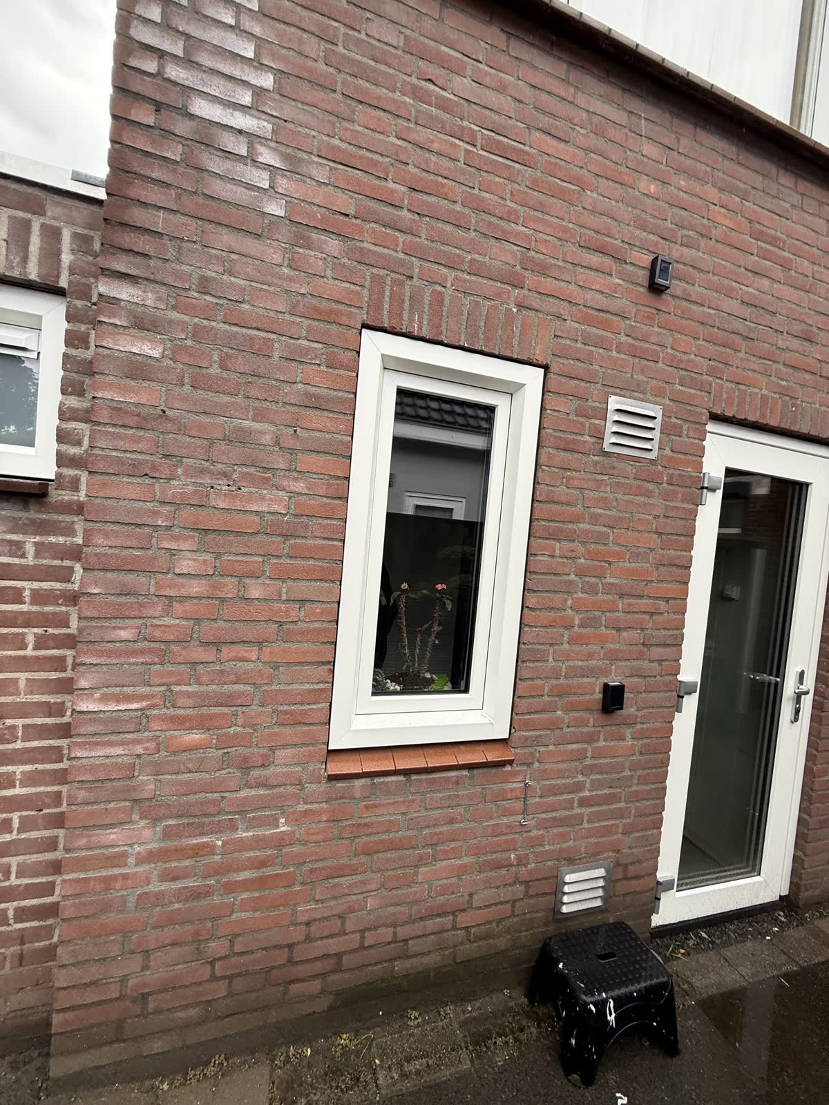 Wit kunststof raam en een witte deur met glas in een gevel van rode baksteen