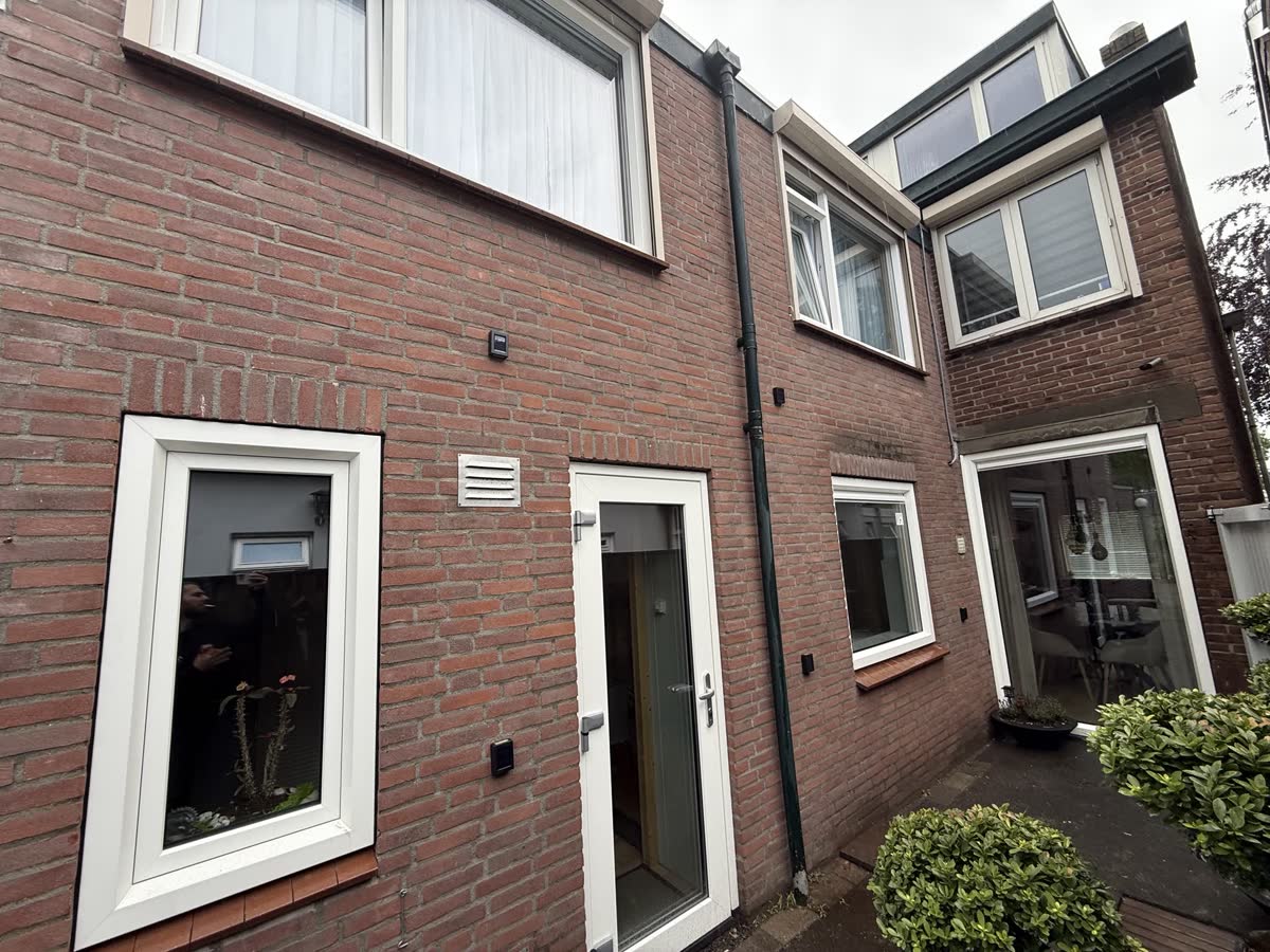 Achterzijde van een bakstenen woning met witte kunststof ramen en een witte achterdeur
