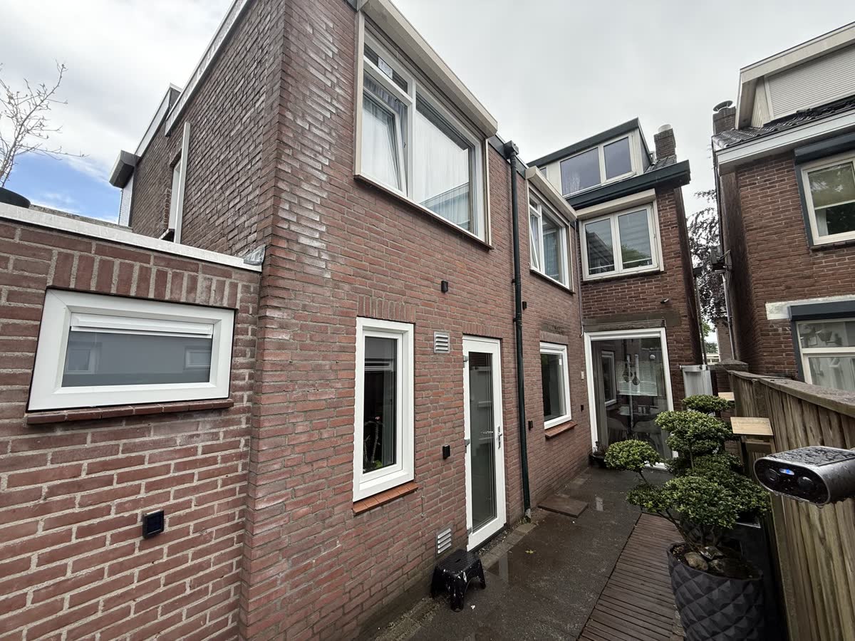 Achterzijde van een woning van rode baksteen met witte kunststof ramen, een witte achterdeur en een laag raam in de aanbouw