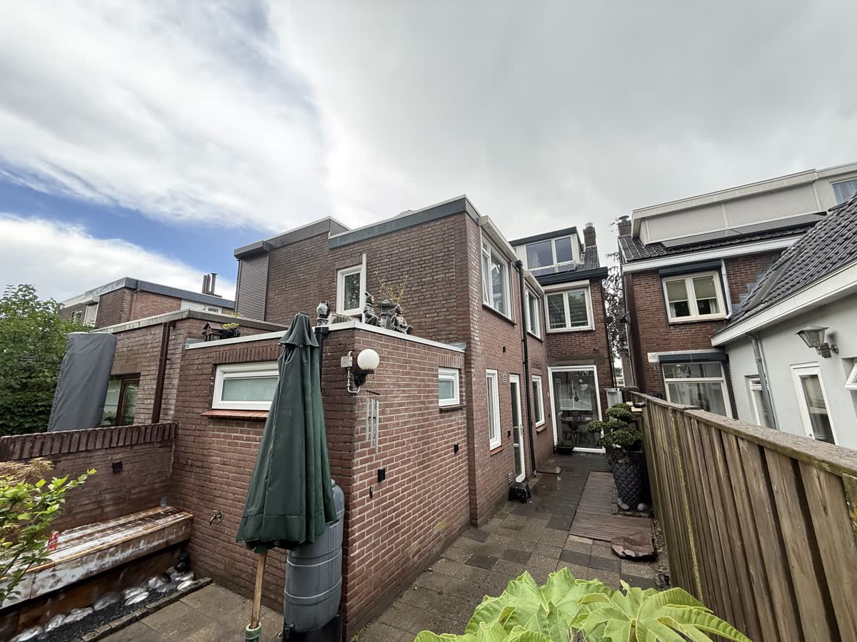 Achterplaats tussen bakstenen woningen met witte kunststof kozijnen en een groene parasol