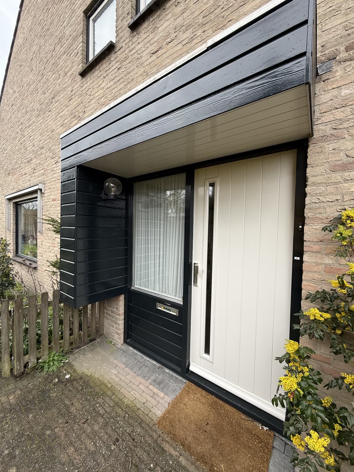 Crèmekleurige voordeur met donker kozijn en zijlicht