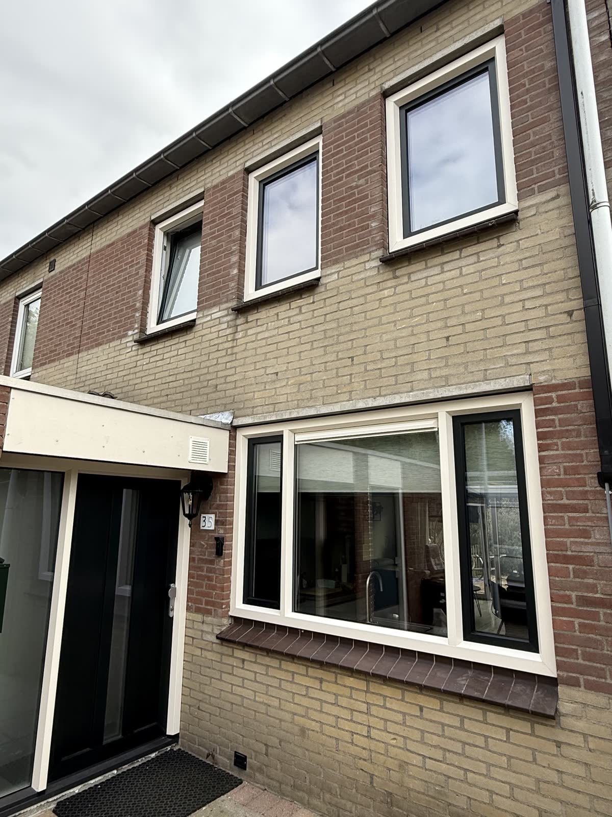 Voorgevel van een rijtjeshuis met crèmewitte kunststof ramen boven en beneden en een donkere voordeur