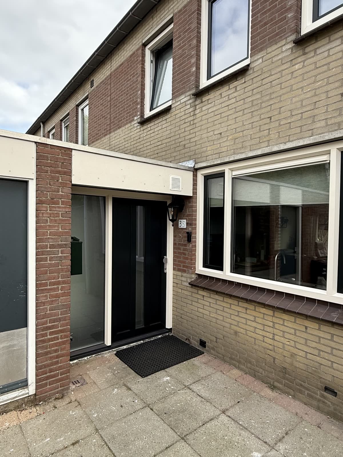 Witte kunststof ramen en een zwarte voordeur met matglazen zijlicht in een gevel van gele en rode baksteen
