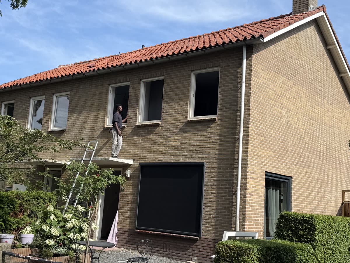 Monteur op een ladder werkt aan de ramen op de verdieping van een woning van gele baksteen