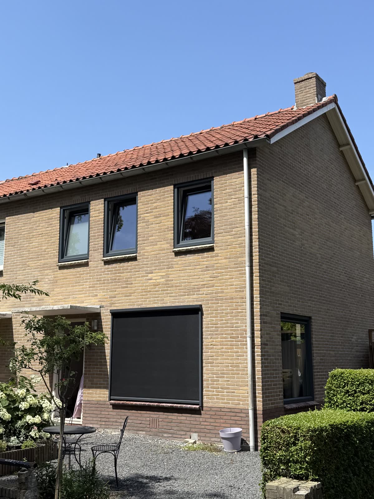 Woning van gele baksteen met donkere kunststof ramen op de verdieping
