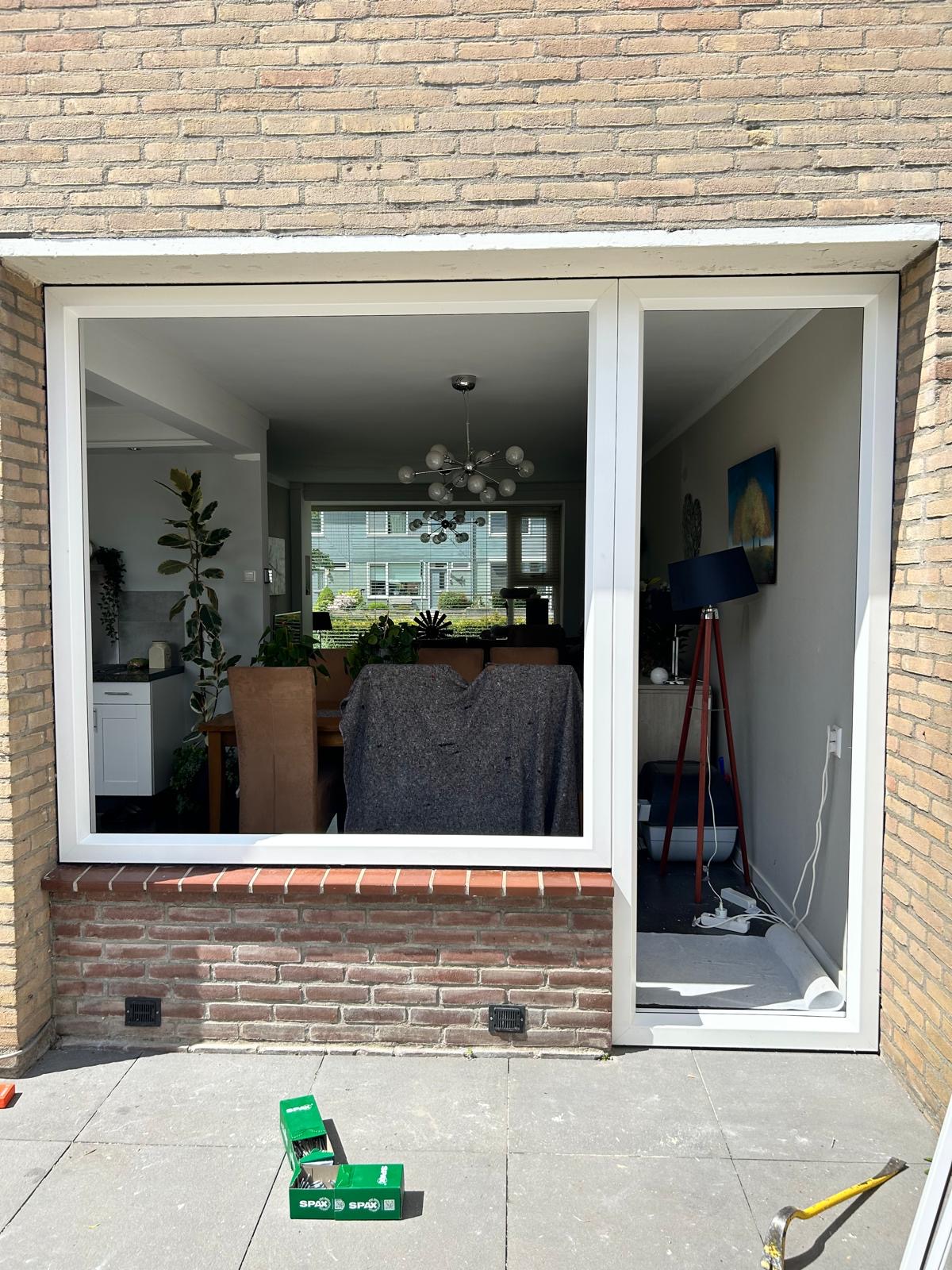 Wit kunststof raam met een deur ernaast in een gele bakstenen gevel