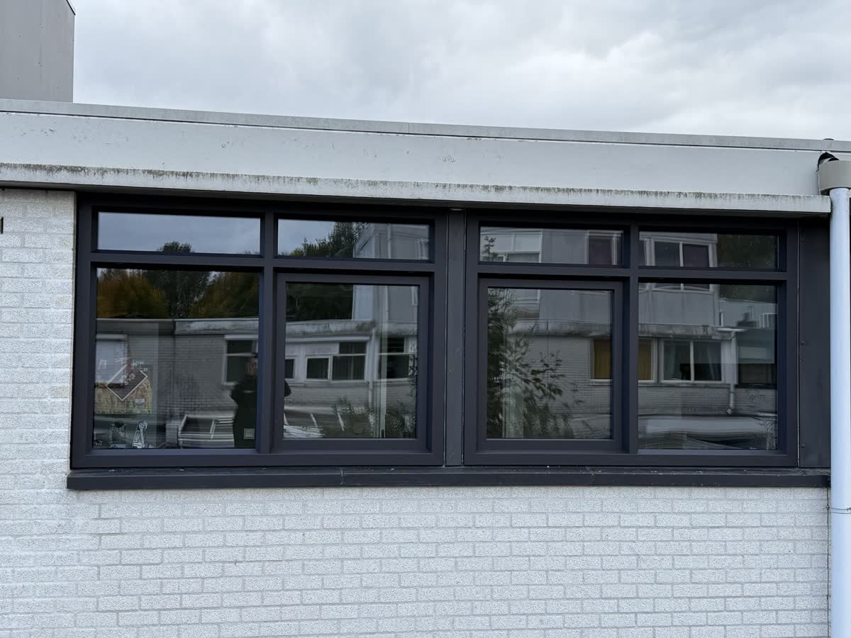 Antraciet kunststof raambanden in een wit gebouw met plat dak