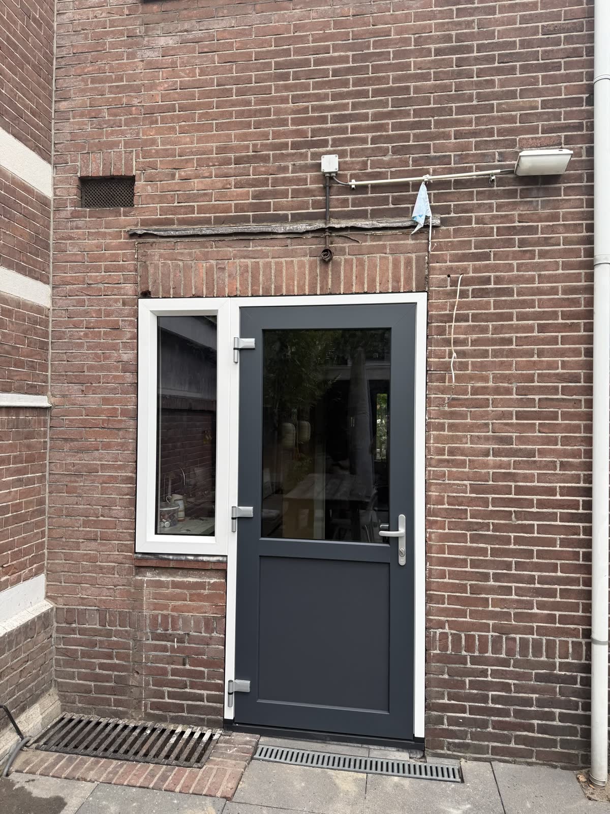 Antraciet kunststof achterdeur met glas in een bakstenen gevel