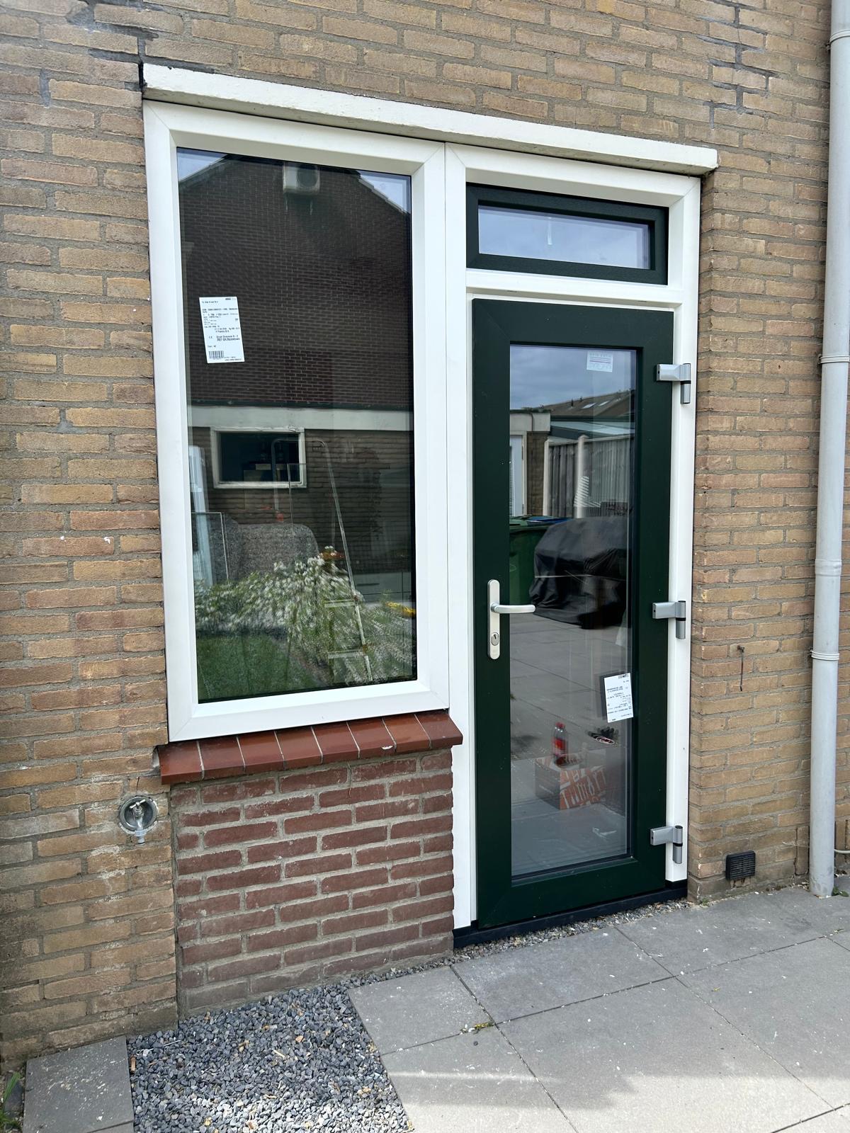 Groene voordeur met bovenlicht naast een wit raam