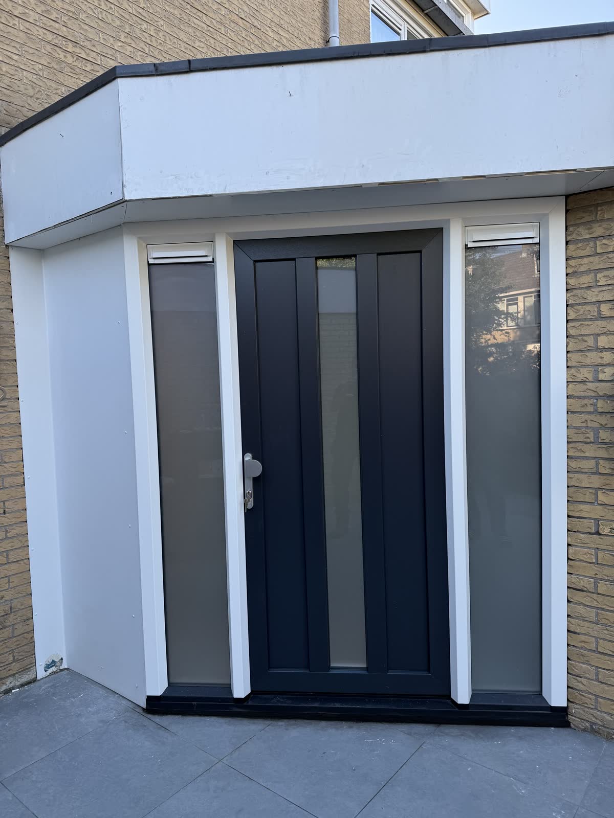 Antraciet kunststof voordeur met zijlichten in een witte portiek