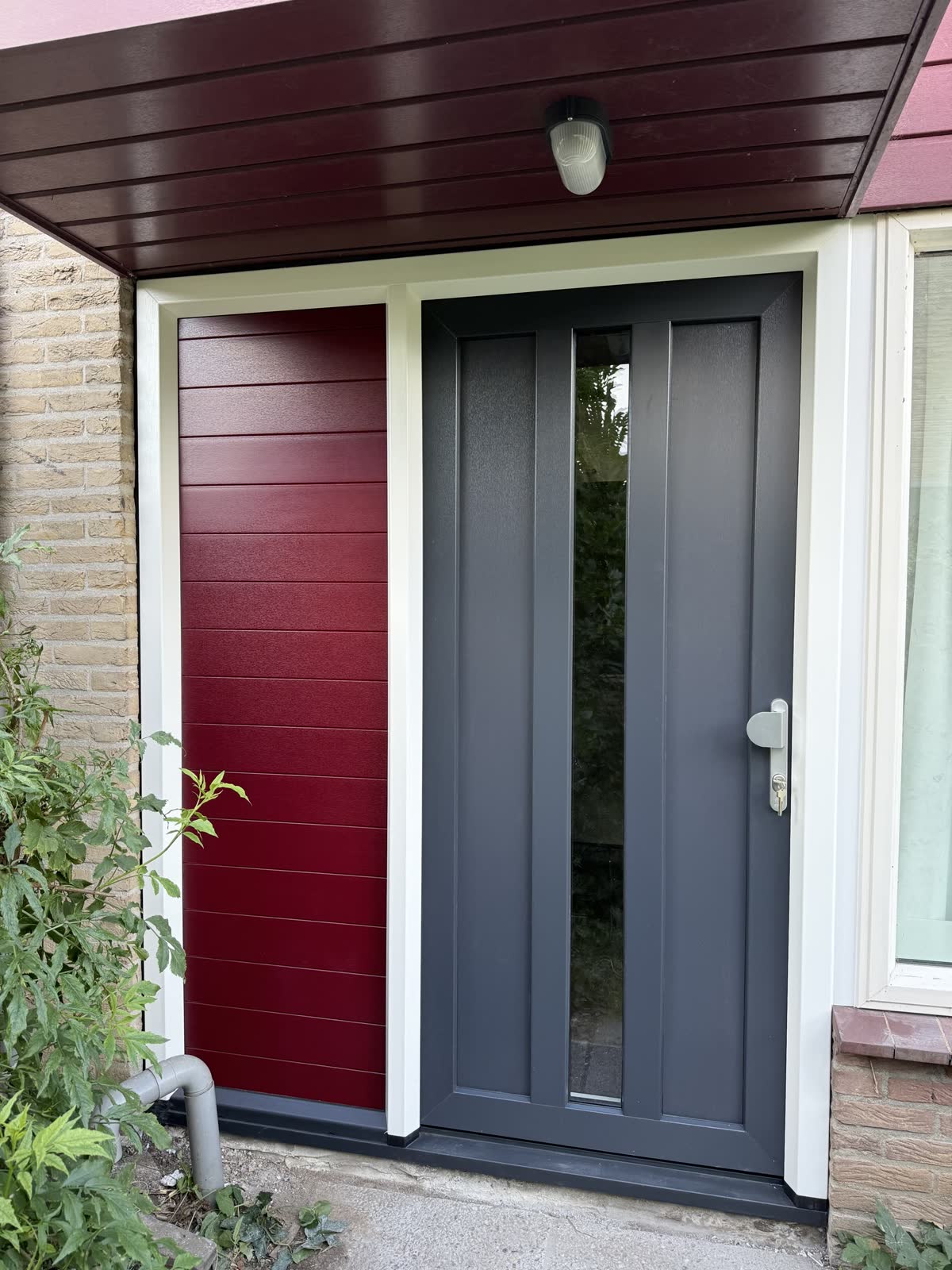Antraciet kunststof voordeur met smalle glasstroken naast een rood paneel