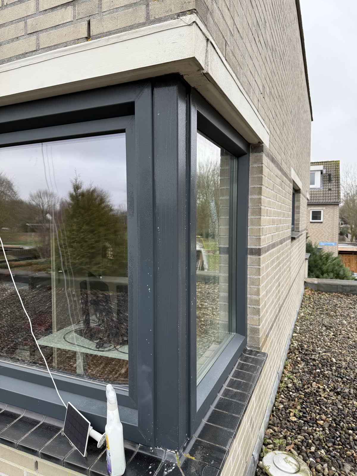 Antraciet kunststof hoekraam met grote glasvlakken op de hoek van een woning